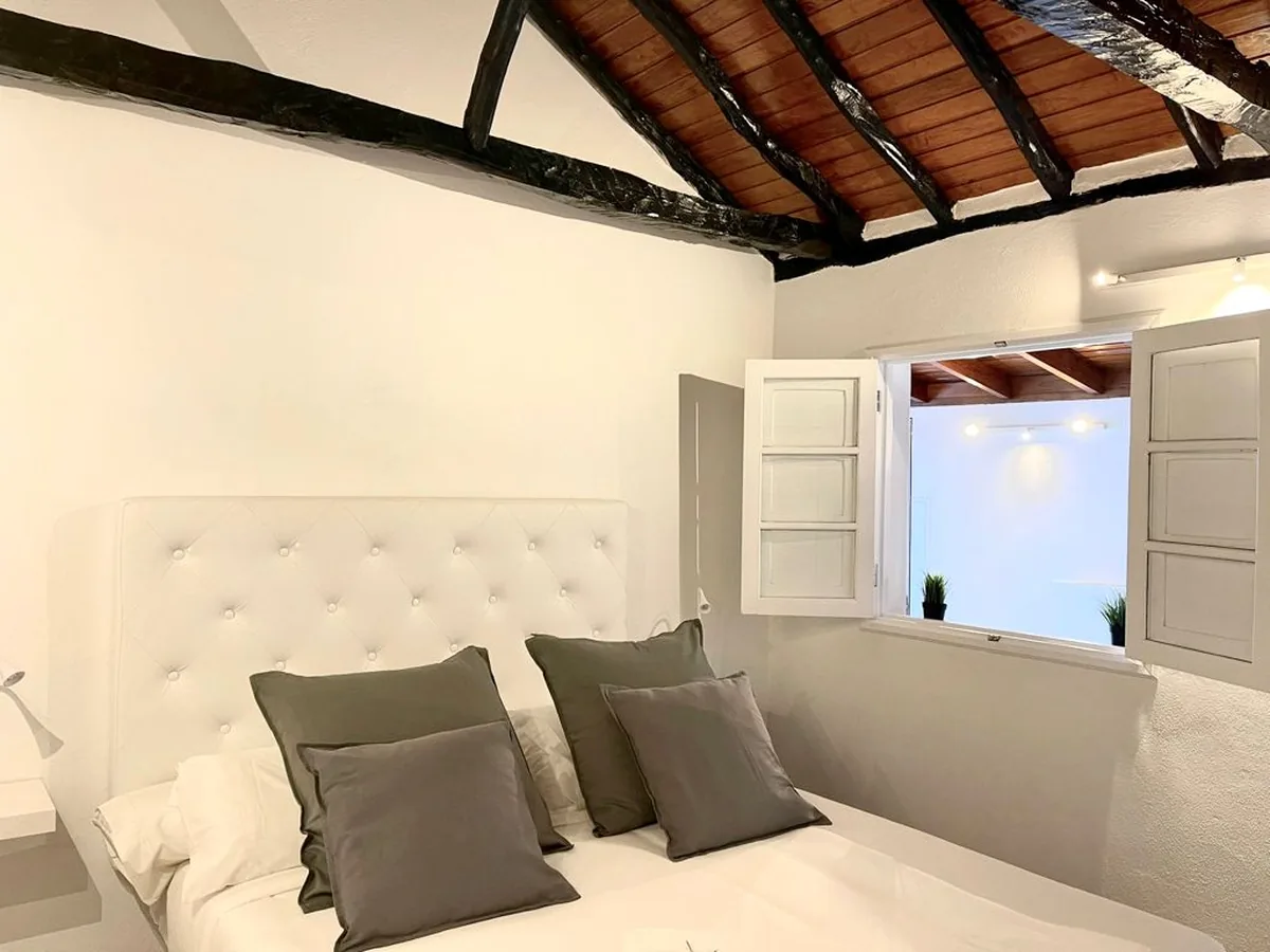 Dormitorio con techo de madera vista y ventana con contraventanas